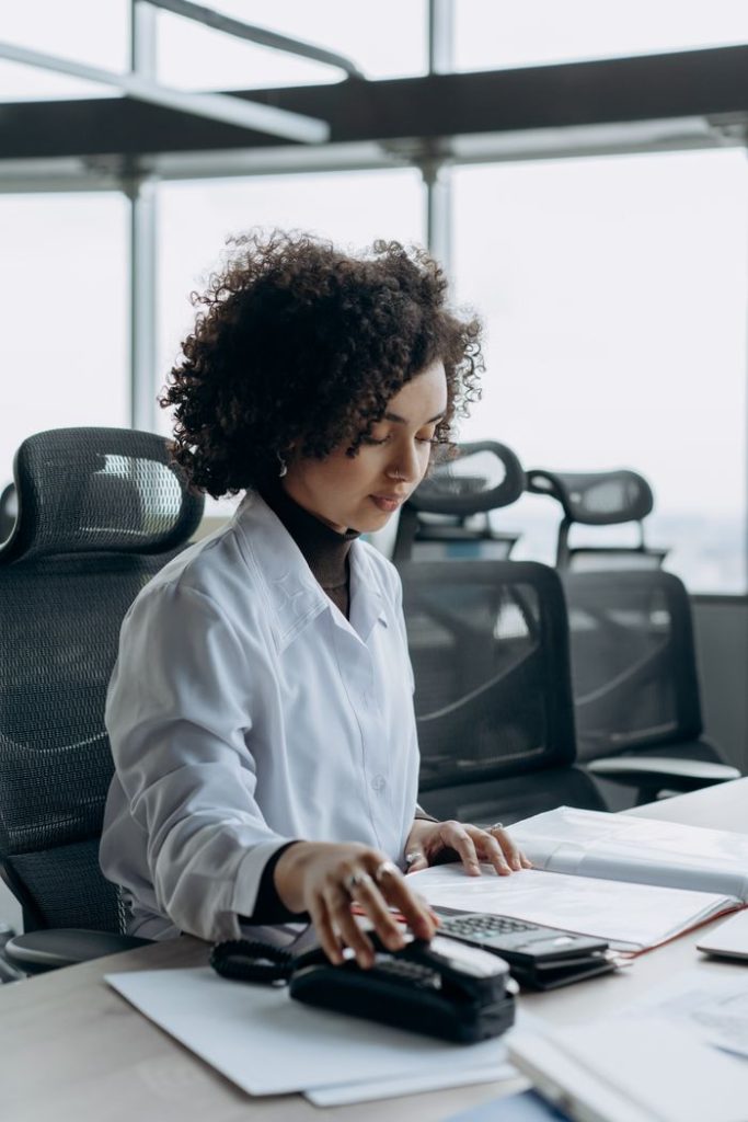 Young woman with curly hair working at a modern office desk, calculating numbers with focus.